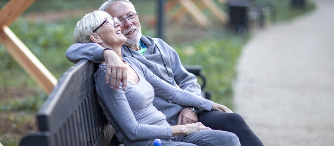Mature couple sitting at banch in park and having fun